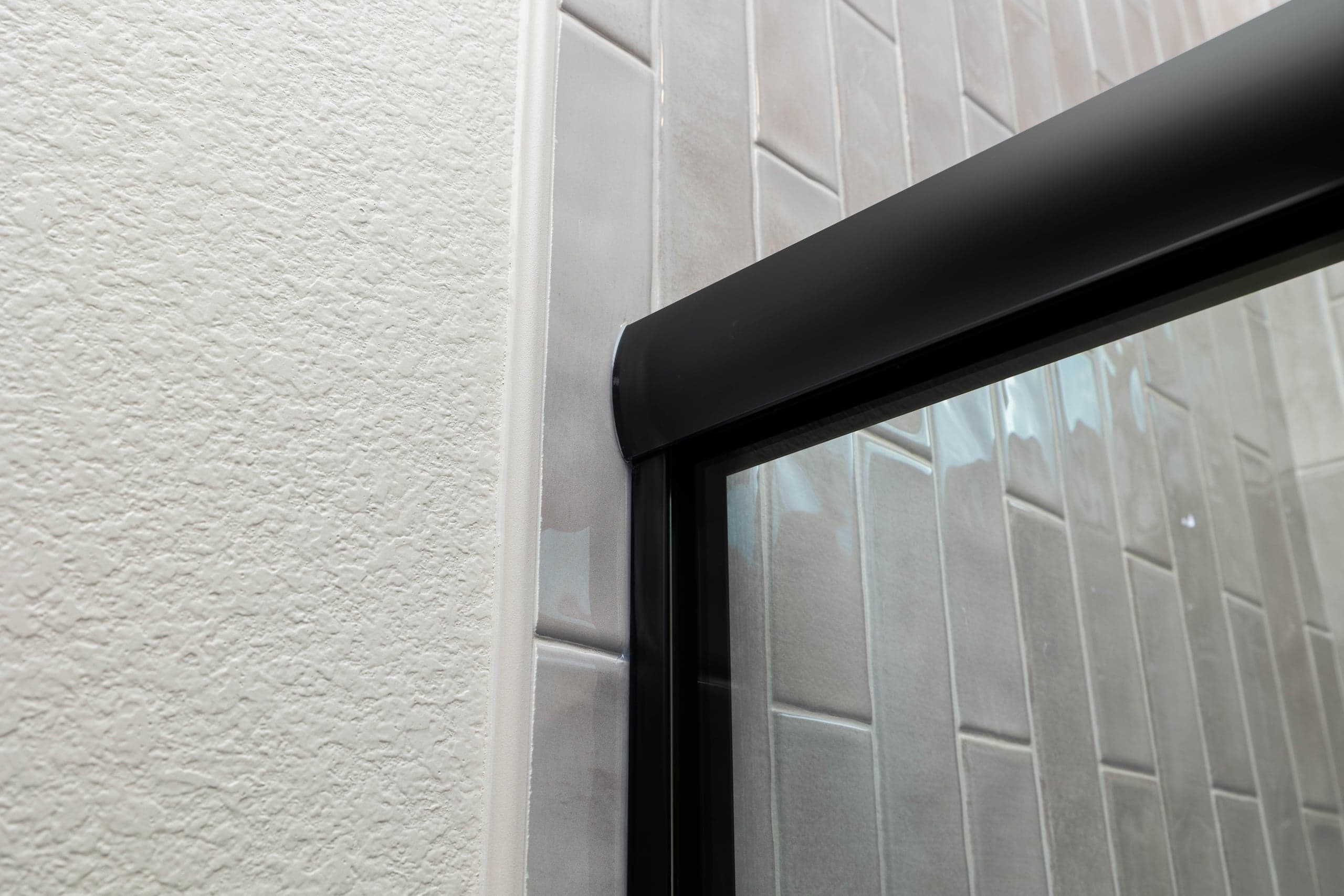 Corner detail of a black-trimmed frameless shower panel meeting the wall on an Infinity Glass and Glazing installation