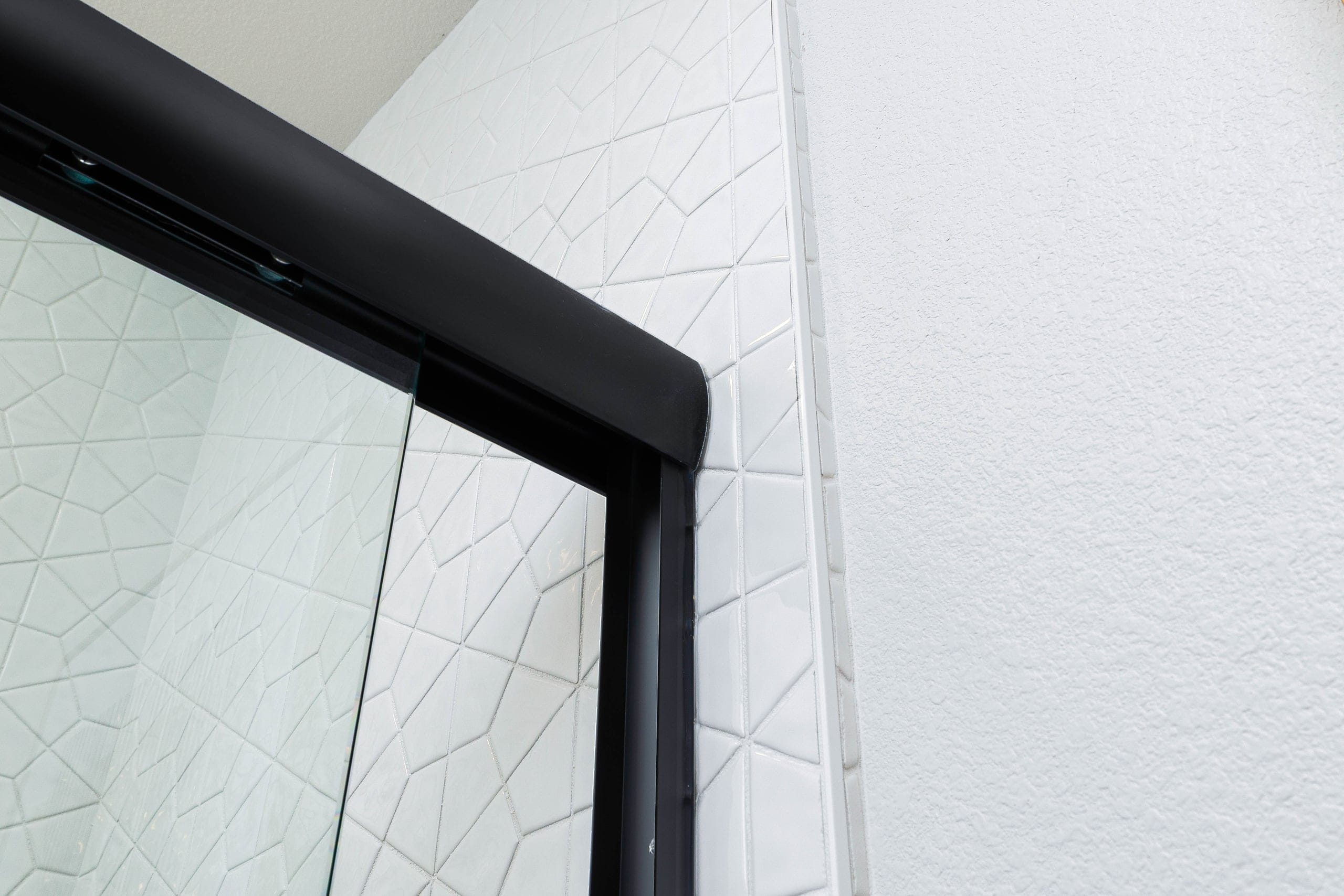 Close-up of black trim on a frameless shower door corner against subway tile