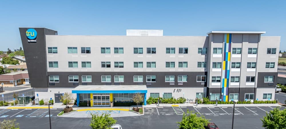 Four-storey Tru by Hilton hotel exterior showing punched window glazing across the full elevation and storefront glass at the entry canopy