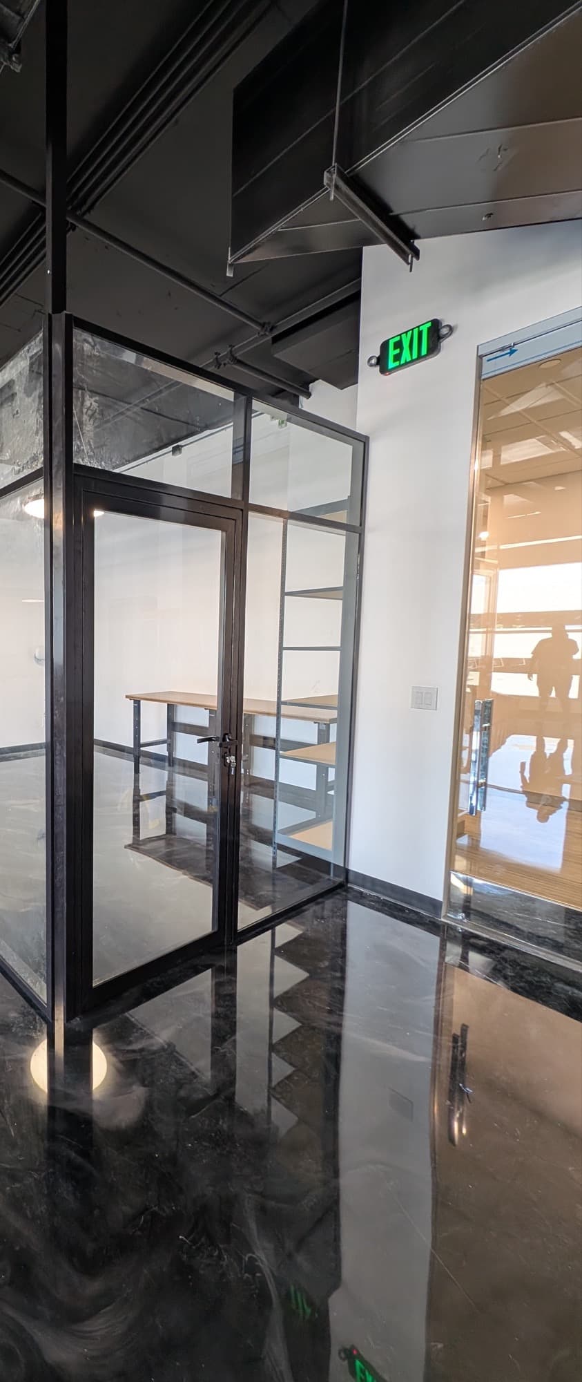 Private office with clear glass walls and a framed glass door in a black frame under an exposed ceiling in downtown Frisco