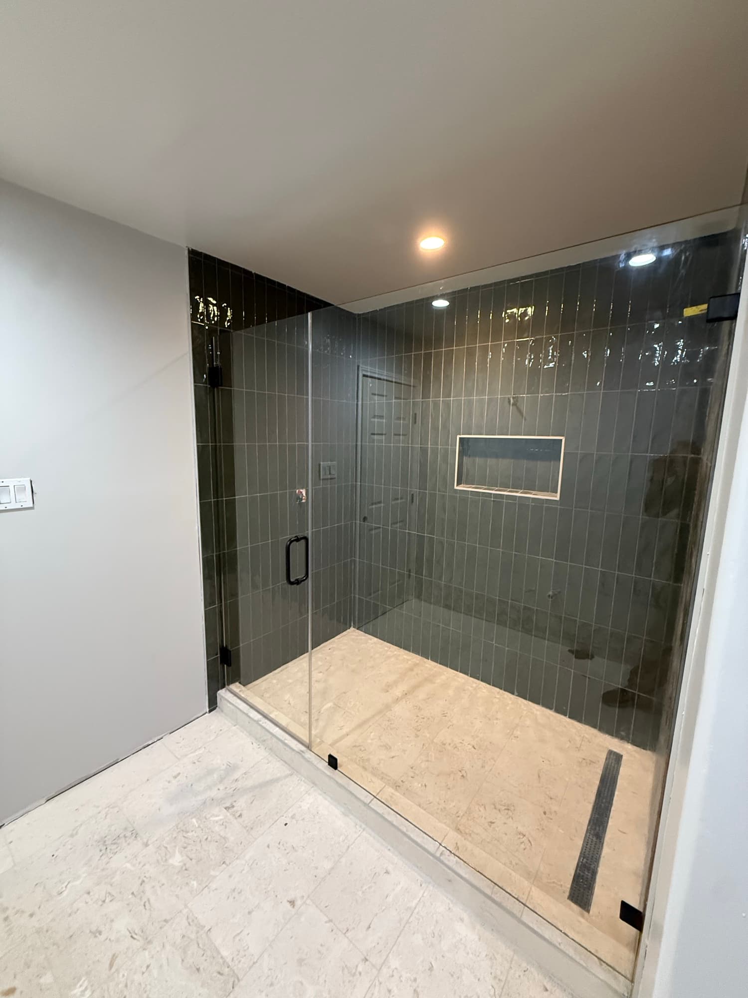 Frameless glass shower with a hinged door and matte black hardware against dark vertical tile in a North Dallas bathroom