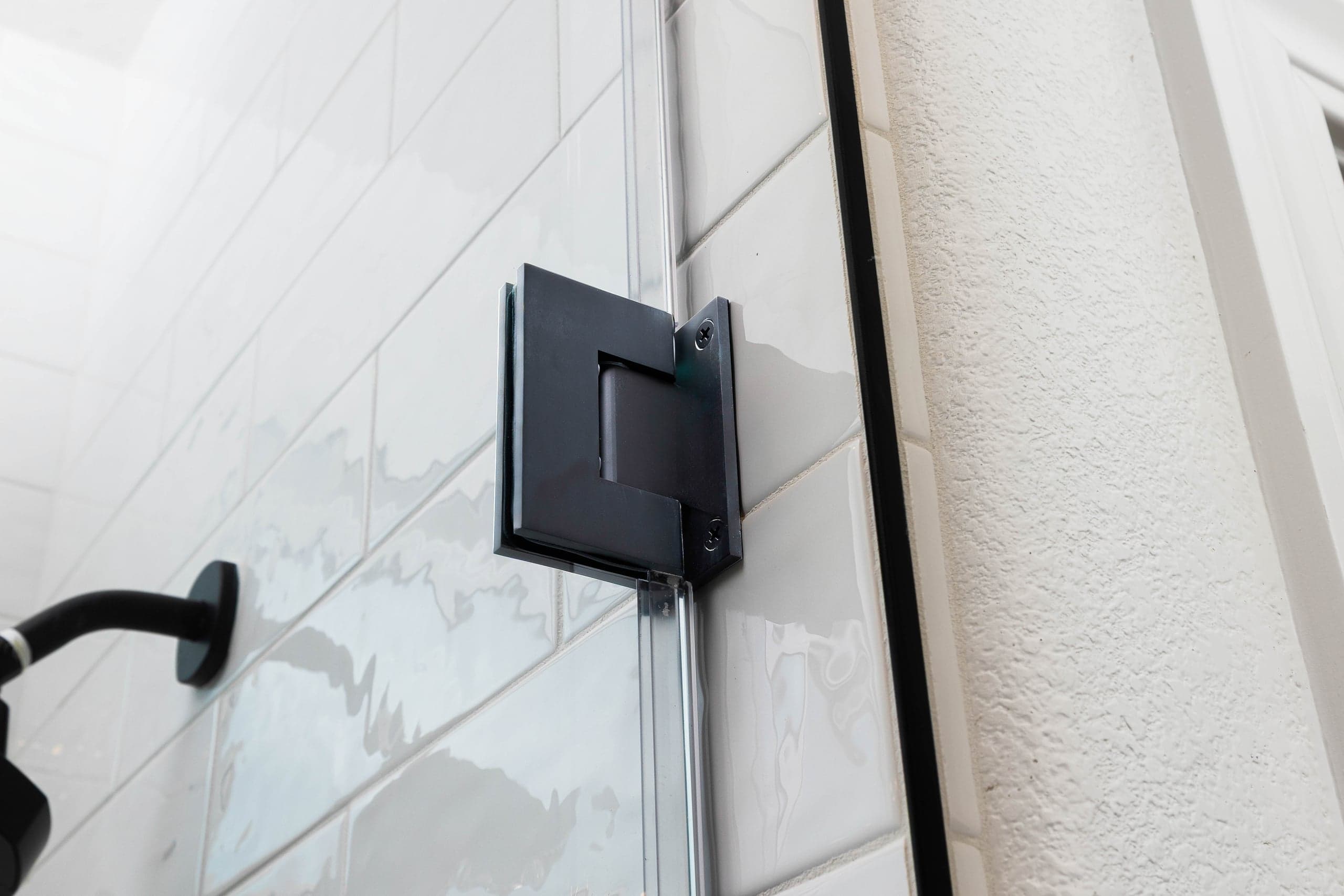Matte black wall-mount hinge holding a frameless shower glass door on an Infinity Glass and Glazing installation